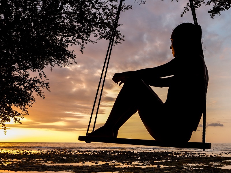 coping with guilt in addiction recovery woman sitting on swing at sunset